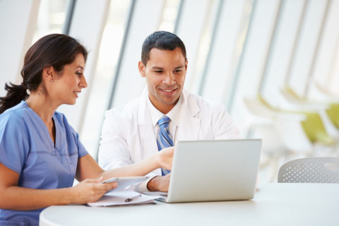 A doctor and nurse look at healthcare data on a laptop